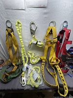 Full view of multiple safety harnesses and straps laid out: yellow, red, and green straps with metal hardware and coiled lanyards.