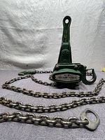 Front side view of green cast lever chain hoist with chain and hook extended.
