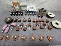 Various sanding and grinding wheels including mounted points, flap wheels, sanding drums, wire brush wheels, and grinding discs arranged on a gray fabric surface.