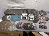 Image showing the full laid out assortment of steel cutting and grinding disks on a table, arranged in groups by type and brand.