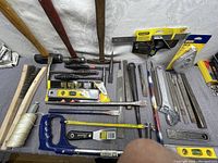 Overview of mostly hand tools arranged on table including hammers, files, scrapers, chisels, a hacksaw, and measuring tape