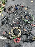 Wide view showing multiple coiled welding cables of various sizes and colors with attached connectors and clamps laid on pavement