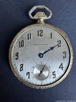 Front face of a vintage South Bend pocket watch with black Arabic numerals, blue hands, no glass.