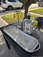 Photo showing the long hammered pewter platter, empty Dos Artes tequila bottle, and brass towel holder arranged on a black table outdoors.