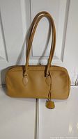 Front view of caramel Furla leather purse with long shoulder straps and leather tag detail.