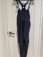 Full view of navy blue Wilfred sleeveless jumper with bib pocket and drawstring waist hanging on hanger.
