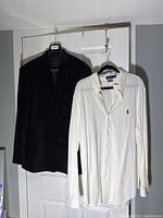Photo showing the black velvet blazer and white Ralph Lauren Polo shirt hanging on hangers against a door.