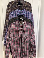 Four plaid long sleeve men's shirts hanging on hangers showing colors and patterns
