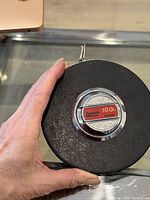 Top view of vintage Lufkin 100ft HW 226 measuring tape showing black circular textured case with central metal badge.