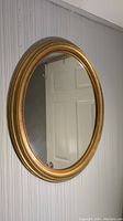 Side angled view of oval gold and bronze finish wall mirror showing frame detail and wear marks.