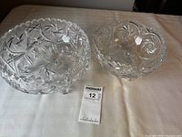 Two crystal serving bowls with distinct cut glass designs placed on a white surface alongside a MaxSold lot number card.