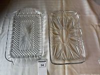 Photo showing two clear rectangular crystal serving trays with different cut glass patterns on a beige surface