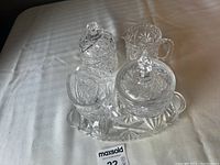 Two sets of crystal sugar and milk serving pieces; one set on an oval crystal tray