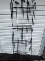 Black metal garden fence panel showing full panel with decorative pointed tops and horizontal wire design against white siding