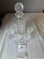 Set of a crystal liquor decanter with stopper and four matching shot glasses on white table.