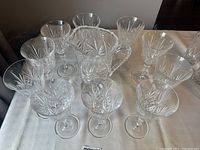Crystal wine pitcher and 10 matching crystal wine glasses displayed on a white cloth, showing intricate cut details.