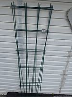 Three green metal garden fence panels leaning against white siding, showing full length and taper shape