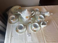 Full tea set including cups, saucers, plates, teapot, milk jug, sugar bowl and serving plate arranged on table.