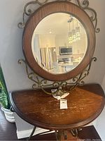 Photo of round wood framed mirror with metal decorative scrollwork above half wood table