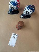 Two miniature hockey goalie helmet collectibles and one small basketball figure shown together on a flat surface
