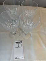 Top-down view of 4 crystal wine glasses arranged in a square formation on a pale tablecloth with a label showing lot info