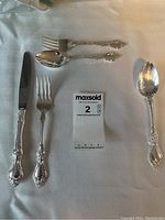 Full set of silver plated cutlery including dinner forks, dessert forks, soup and dessert spoons, and knives arranged on a white cloth.