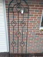 Full view of one tall black metal garden fence featuring an arched top and decorative heart-shaped scrolls.