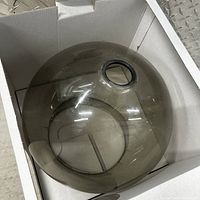 Top-view photo of the round smoky glass pendant light shade inside a cardboard box showing its smooth translucent surface and round shape with central hole.