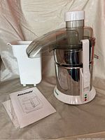 Full view of Juicelady JL500 electric juicer with plastic juice container and instruction manual laid on fabric surface.