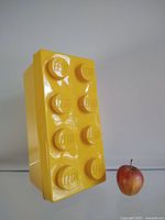Vertical view of the large yellow LEGO brick-shaped storage box with an apple for scale.