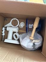 Top view of box containing KitchenAid meat grinder attachment parts, wrench, and Ninja blender components including container and tamper.
