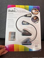 Front view of unopened UltraBrite LED Booklights blister pack with 2 LED booklights and 6 AAA Duracell batteries included, showing product details and colorful packaging.