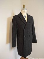 Full-length front view of charcoal gray herringbone overcoat on dress form, showing double-breasted buttons and notch lapels.