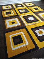 Large linen table cloth laid flat on floor, showing bold concentric squares in yellow, brown, black, and white.