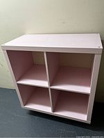 Front view of pink 4-compartment bookcase showing 2x2 square compartments and smooth finish. Visible slight marks on outer surfaces and inside compartments.
