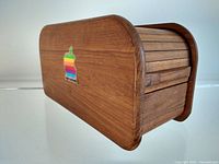 Side view of teak tambour roll top box showing the curved edge and vintage Apple rainbow sticker with slight wear on one edge.