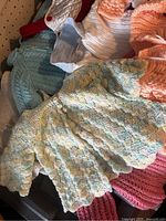 Various pastel and neutral colored vintage baby knit sweaters and a multicolor scalloped knit item laid out on a surface.