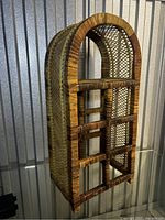 Front angle view showing the curved top and bottle slots of the rattan wine rack.