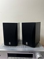 Front view of two rectangular black Yamaha speakers with fabric covers and Yamaha logos, sitting on stereo unit.