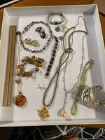 Photo showing a collection of pre-owned vintage jewelry including amber beads, various necklaces, bracelets, earrings, and rings in mixed materials without precious metals.