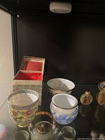 Wide view of Asian art items showing porcelain cups, small glass teapot, and decorative box with felt lining