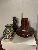 Photo showing three items: Asian bronze vase, large brown pottery vase, and ceramic elephant figurine.