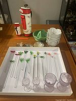 Photo of full assortment of bar accessories including cocktail shaker, ceramic bowls, glass stirring sticks, and small nut shaped dishes