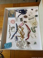 Overview of assorted beads and jewelry components arranged on white surface. Visible strands, loose beads in bags and small containers.