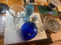 Photo showing three Blenko glass vases, two clear crystal vases, and a glass paperweight on a white surface.