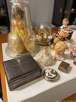 Wide view of collectable dolls, figurines, and trinket boxes including yellow dress doll, wedding topper, and various ceramic busts and boxes.