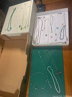 Wide view of costume jewelry box showing assorted necklaces and bracelets arranged on cardboard surfaces.