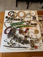 Overview of all costume jewelry items displayed on table, showing full lot content including bracelets, necklaces, and pendants.