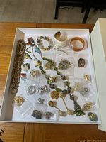 Overview of various costume jewelry items laid out on a white tray highlighting necklaces, Bakelite bracelets, brooches, rings, and pins.