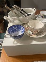 Photo showing two porcelain teacups and a large salt glaze serving bowl with serving utensils.